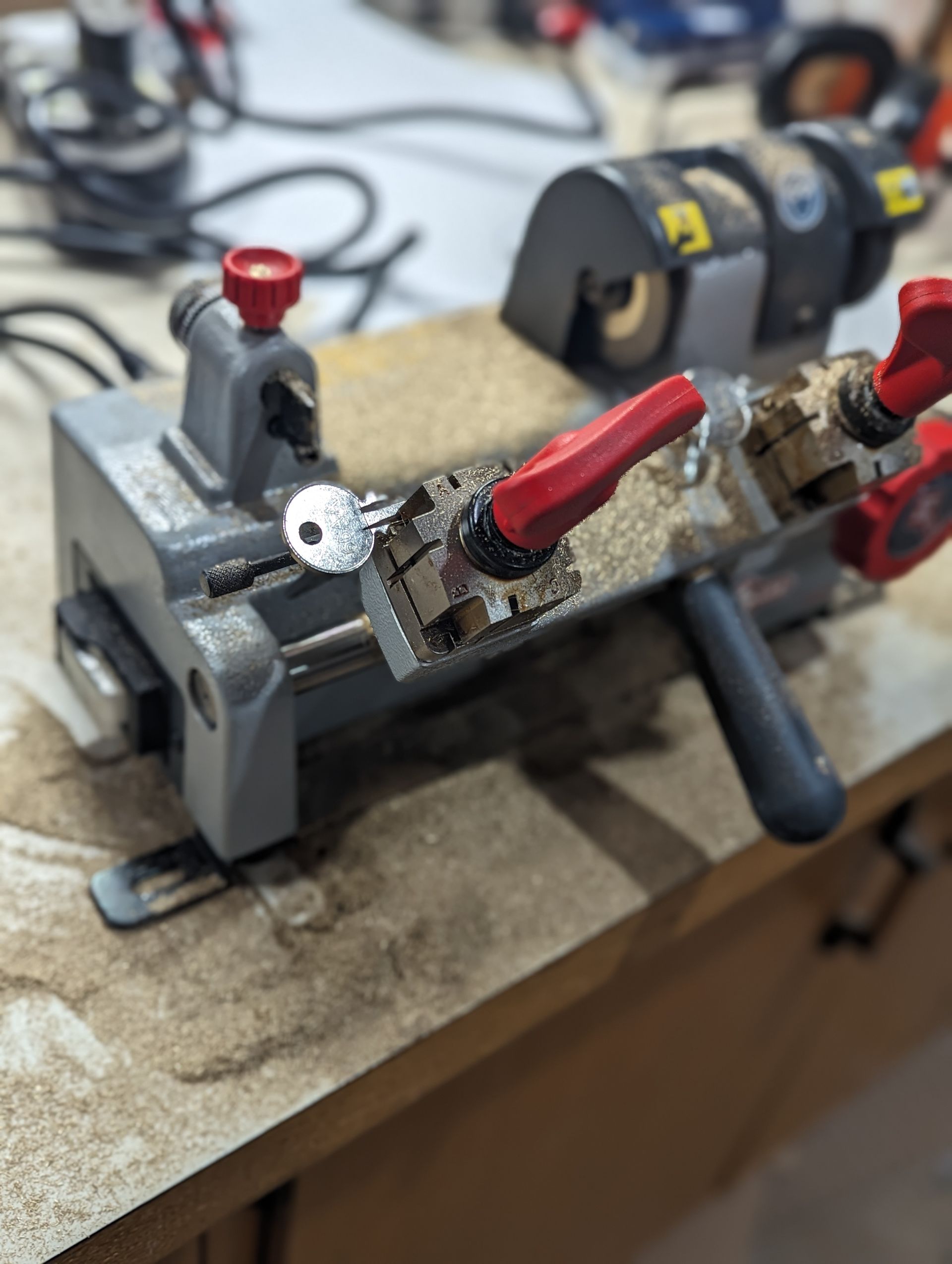 Key being cut by a key-cutting machine. The key is blue and metal shavings are visible.