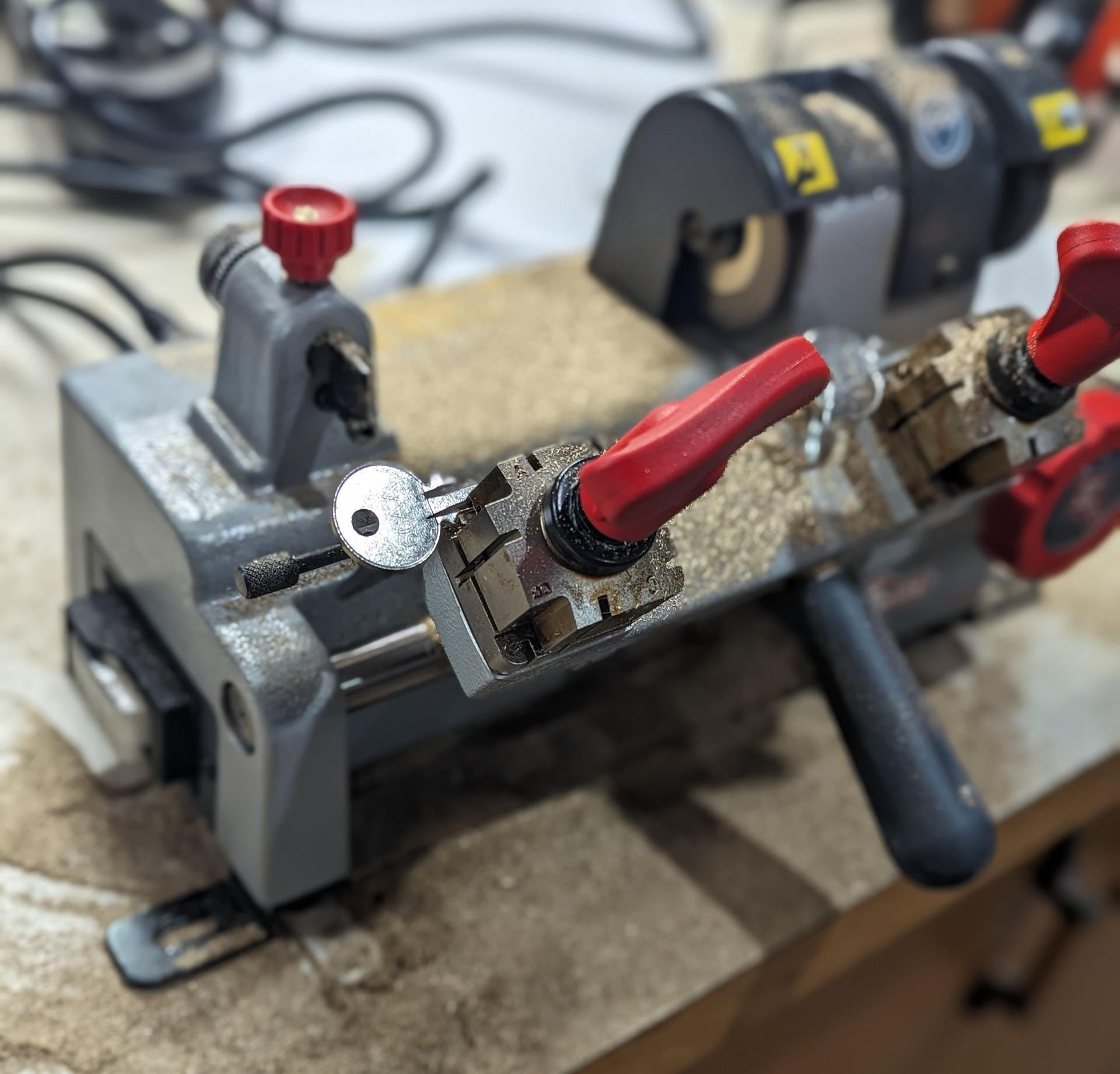 Key being cut by a key-cutting machine. The key is blue and metal shavings are visible.