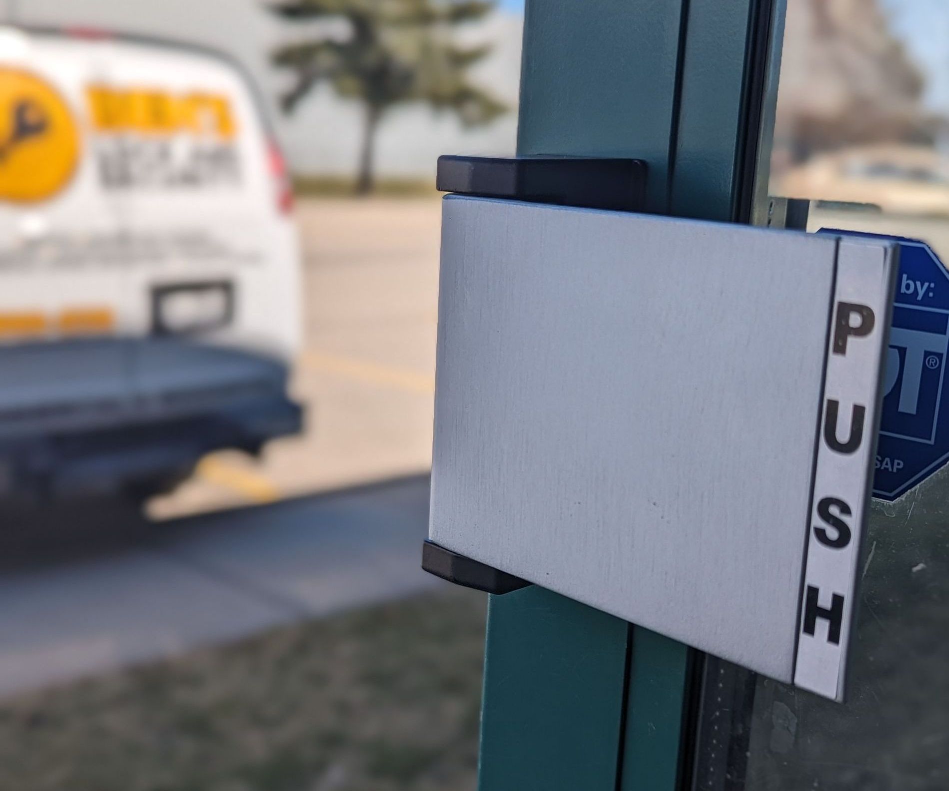 A white van is parked behind a push sign on a door
