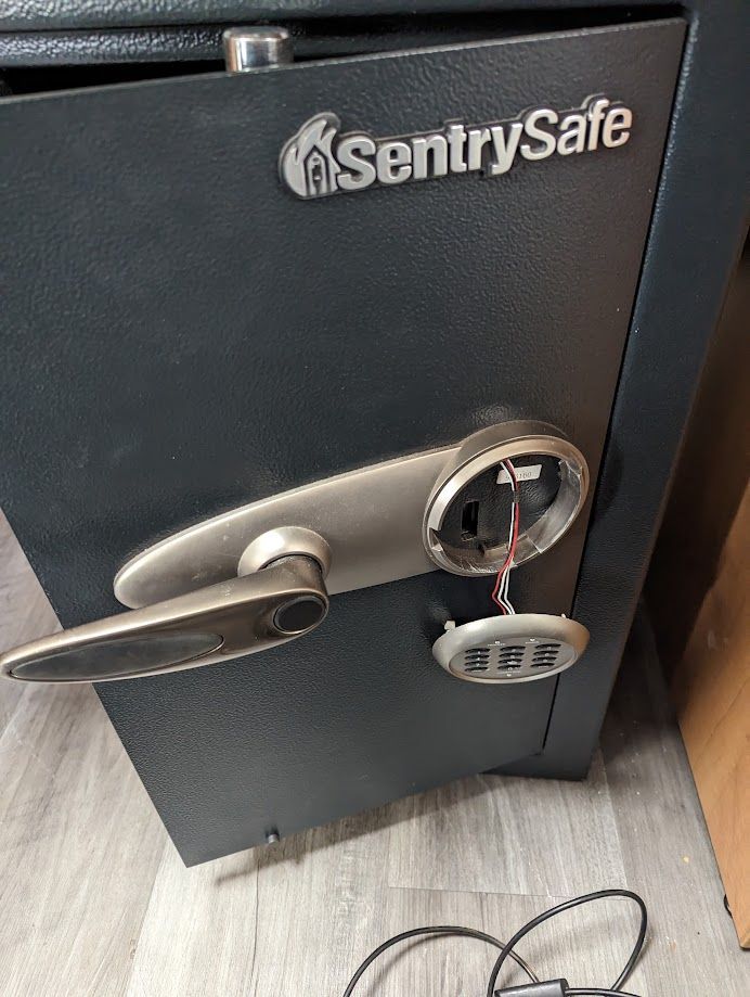 A sentry safe is sitting on a wooden floor next to a cord.