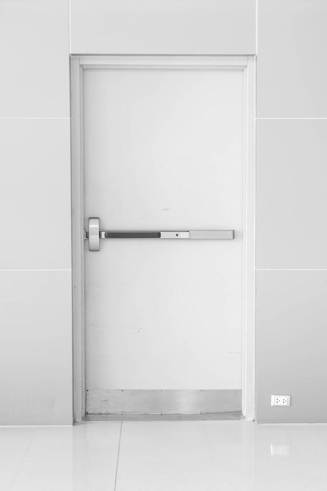 a white door with a panic bar on it is in a white room .