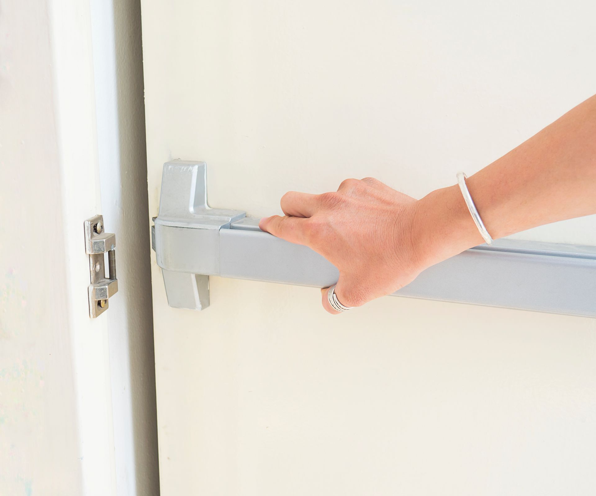 A woman is opening a door with a panic bar.