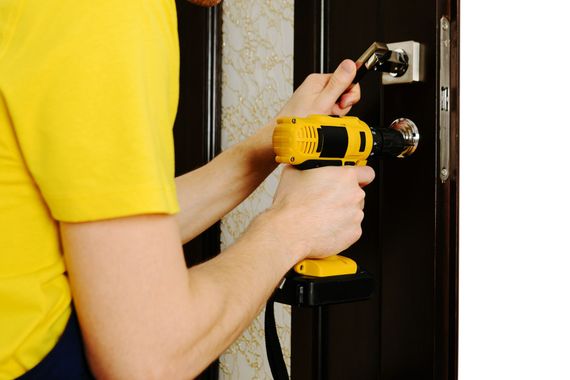 a man in a yellow shirt is using a drill to fix a door .