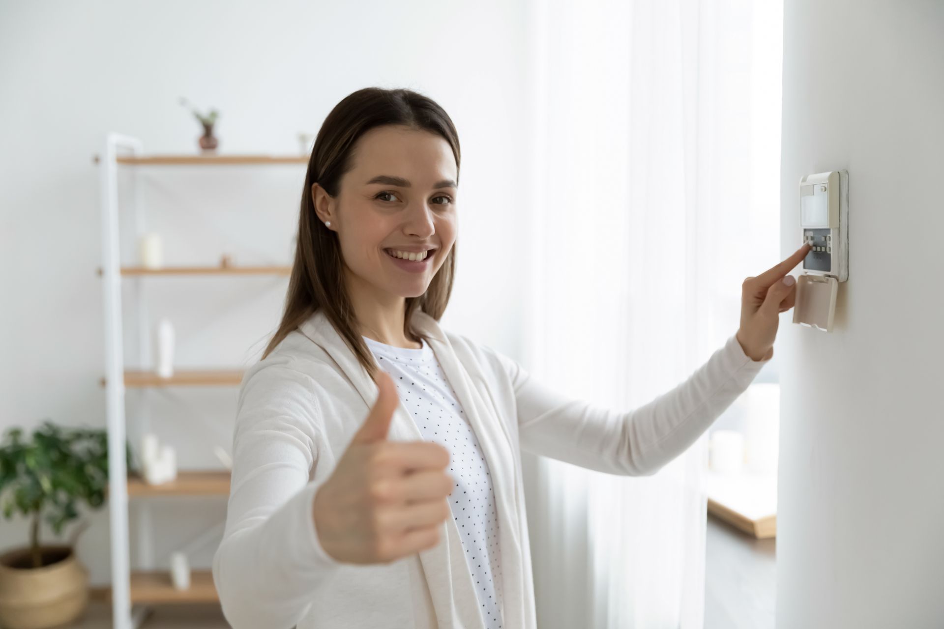 A woman is giving a thumbs up while using a security system.