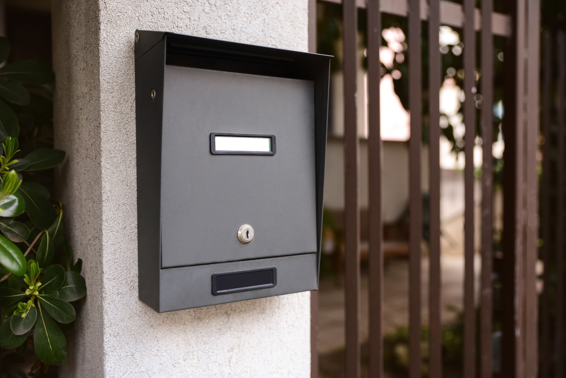 A mailbox is attached to a wall next to a fence.