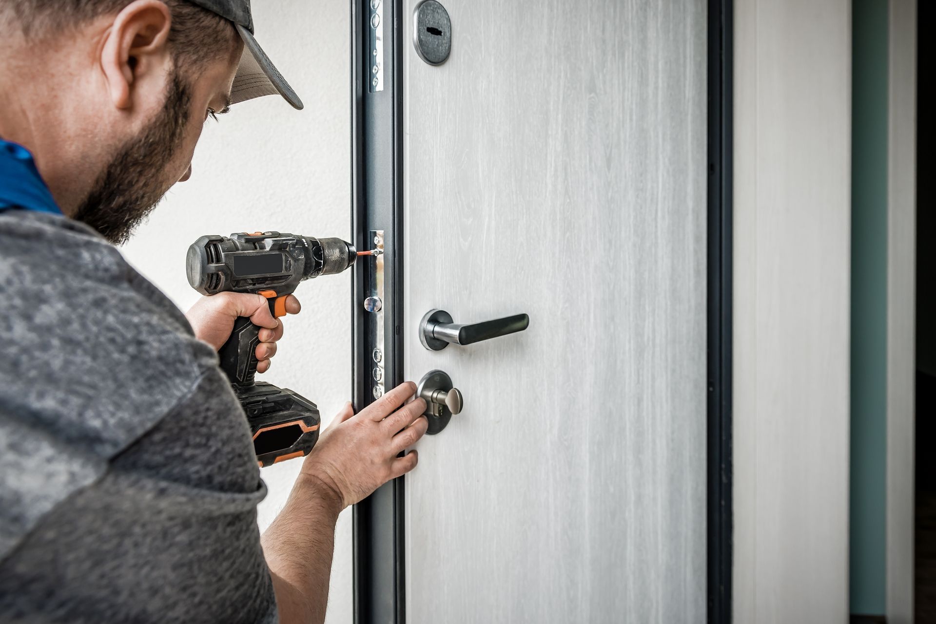 Person using a drill to install a door lock on a white door.