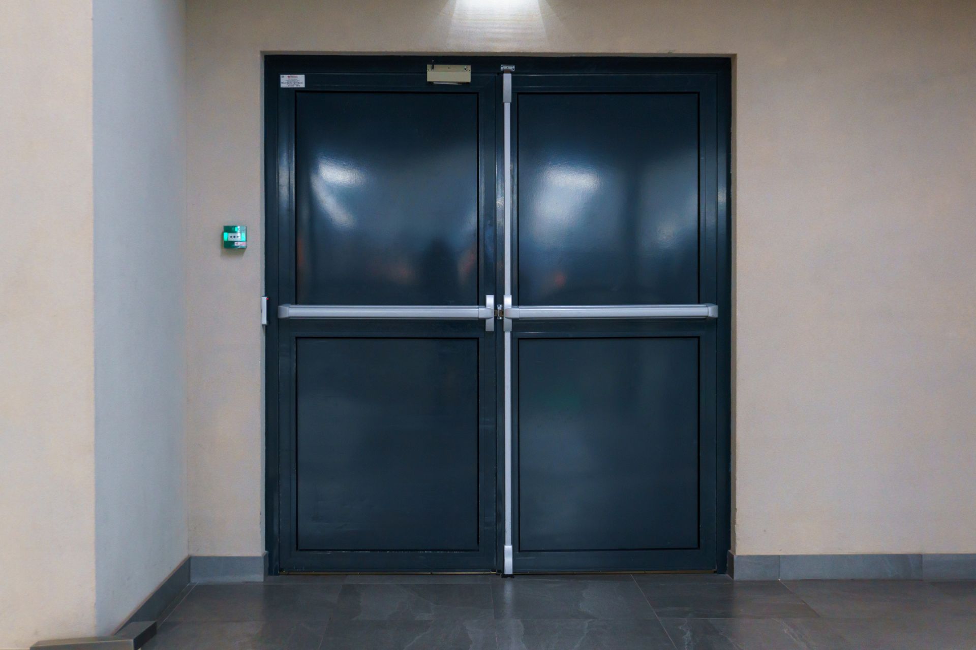A pair of black doors in a building with a green light on the wall.