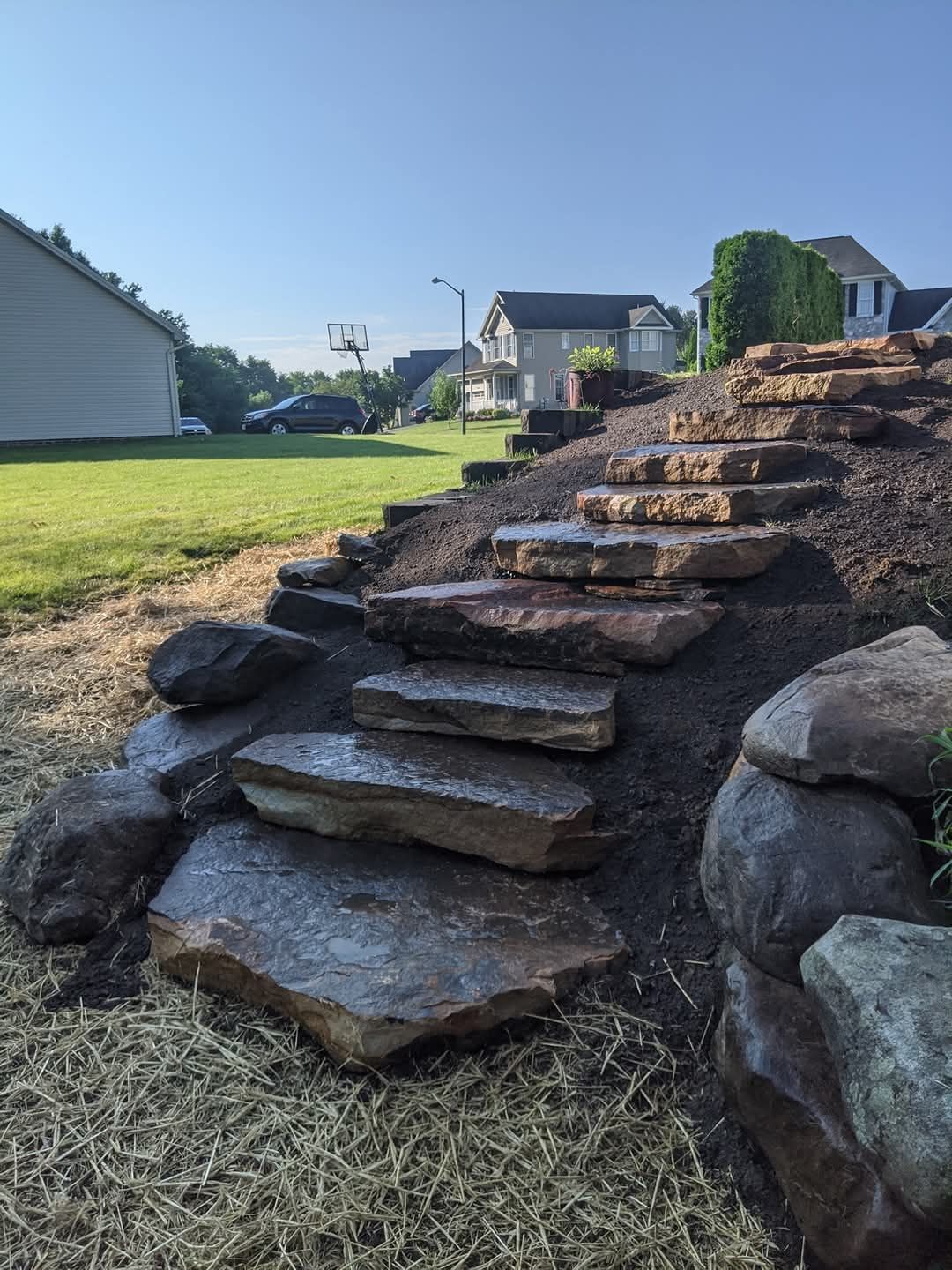 Jesse James Hardscaping - Stone steps lead up a hill in a yard, near houses.
