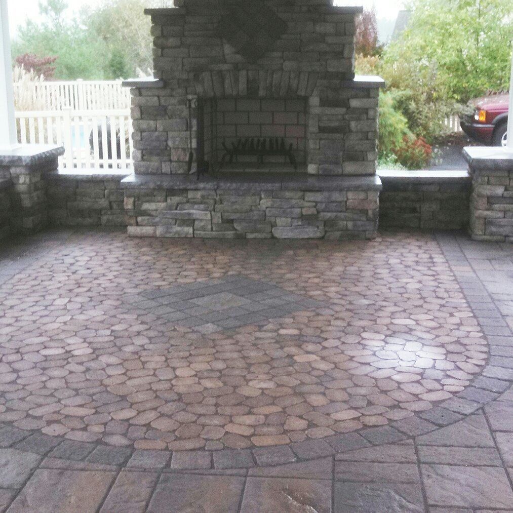 Jesse James Hardscaping - Stone patio with fireplace, circular brick pattern, and rectangular border.