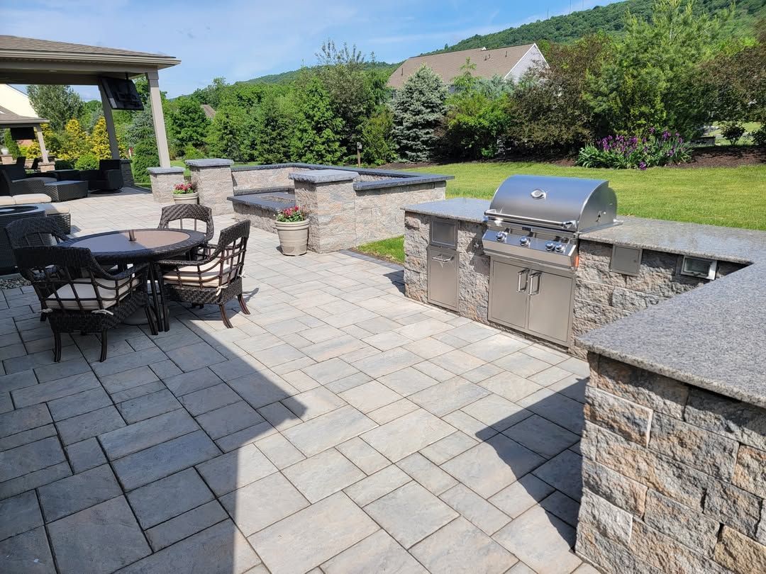 Jesse James Hardscaping - Outdoor patio with a grill, stone countertop, dining set, and lawn.