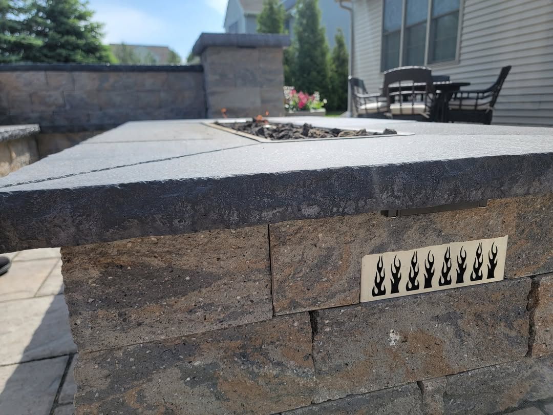 Jesse James Hardscaping - Outdoor stone fire pit with decorative tile and seating area.