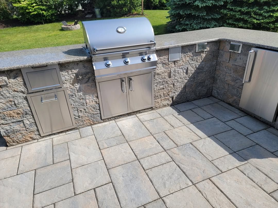 Jesse James Hardscaping - Outdoor kitchen with stainless steel grill, appliances, and stone patio.