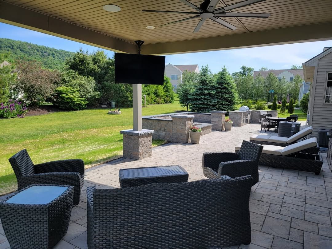 Jesse James Hardscaping - Patio with outdoor seating, TV, and view of a green yard and trees.