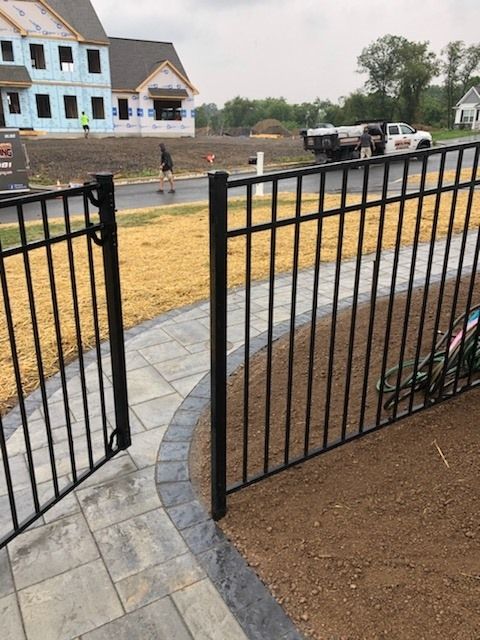 Jesse James Hardscaping - Black metal gate on a brick walkway, leading to a yard with construction in the background.