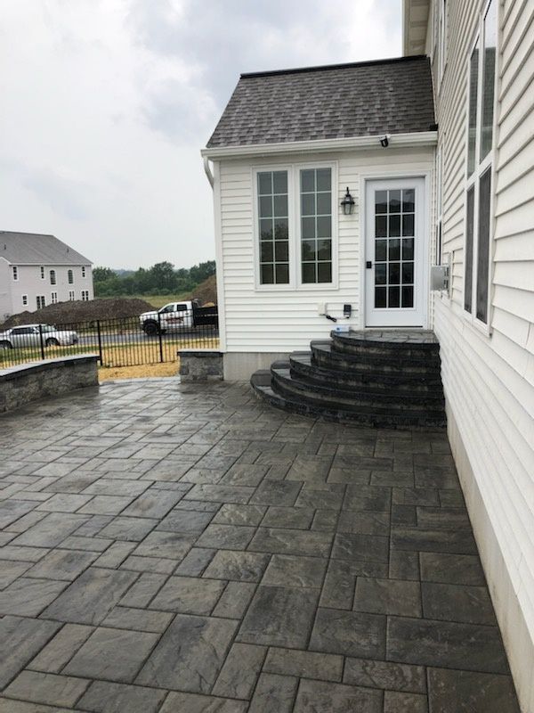 Jesse James Hardscaping - Gray paver patio with steps leading to a white-walled porch with a door.