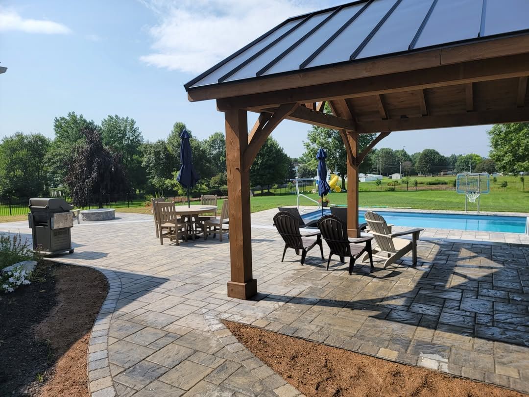 Jesse James Hardscaping - Patio with gazebo, pool, chairs, and dining table. Sunny day, outdoor setting.