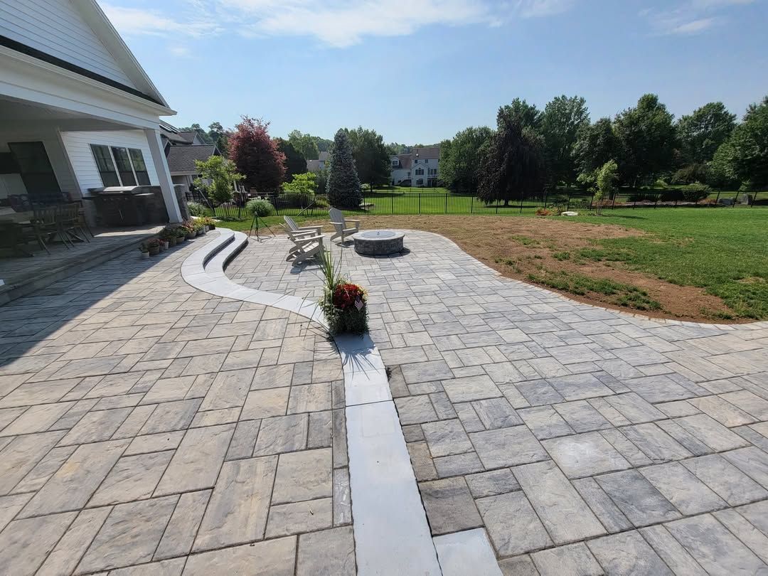 Jesse James Hardscaping - Backyard patio with light gray paving, a house, and green grass under a blue sky.