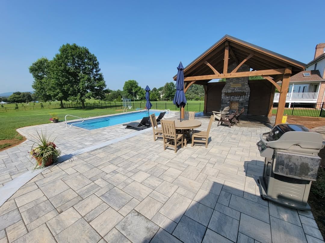 Jesse James Hardscaping - Backyard patio with pool, table, grill, and gazebo under a blue sky.