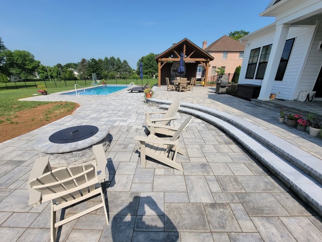 Jesse James Hardscaping - Patio with chairs, fire pit, and pool. People working on a gazebo near a house on a sunny day.