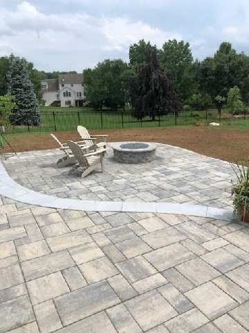 Jesse James Hardscaping - Patio with stone pavers, fire pit, and Adirondack chairs; backyard setting.