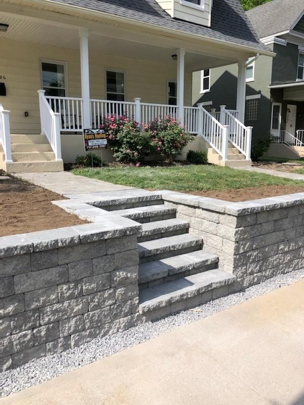 Jesse James Hardscaping - Stone steps lead up to a house with a white porch and a yellow exterior.