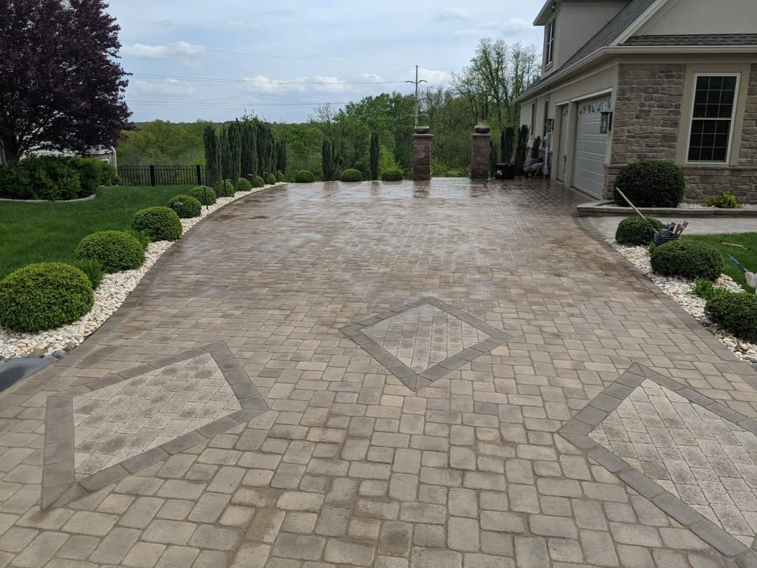 Jesse James Hardscaping - Stone block driveway leading to a house with decorative diamond inlays and landscaping.