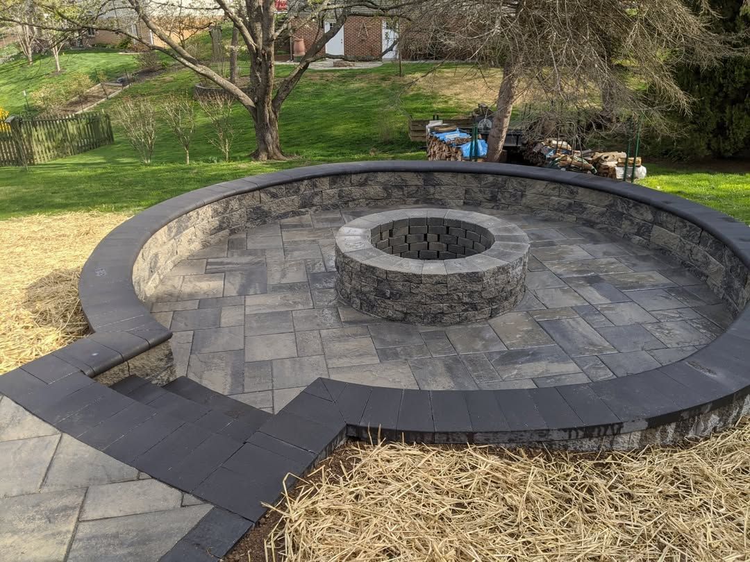 Jesse James Hardscaping - Circular stone fire pit with surrounding seating area on a paved patio.