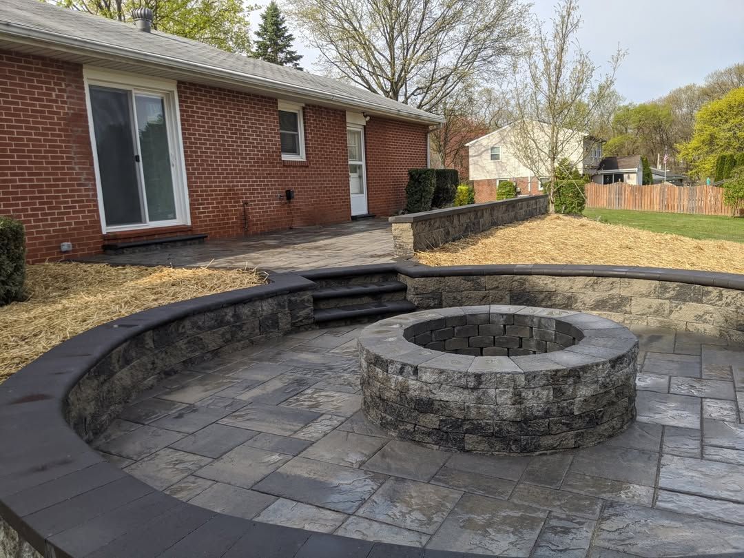 Jesse James Hardscaping - Brick home with paved patio, fire pit, and steps leading up to a grassy area.