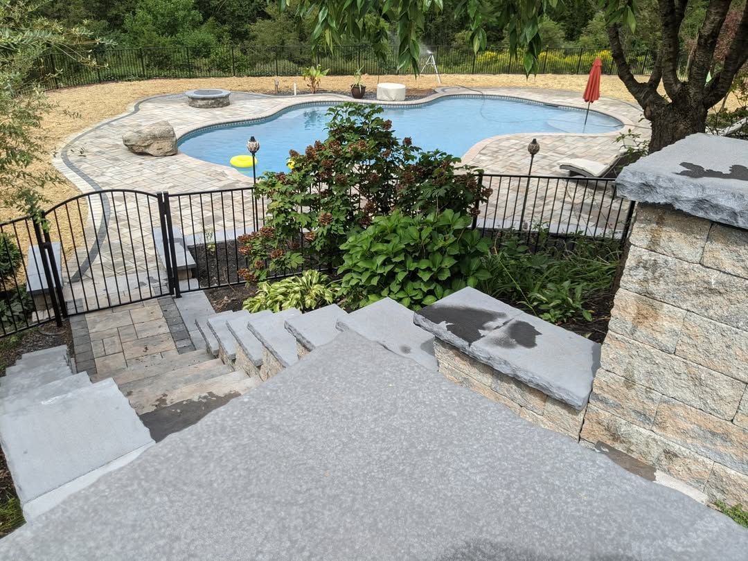 Jesse James Hardscaping - Steps leading down to a pool, fenced with stone walls and lush green plants.