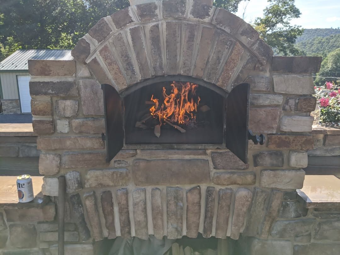 Jesse James Hardscaping - Stone outdoor pizza oven with fire burning inside.