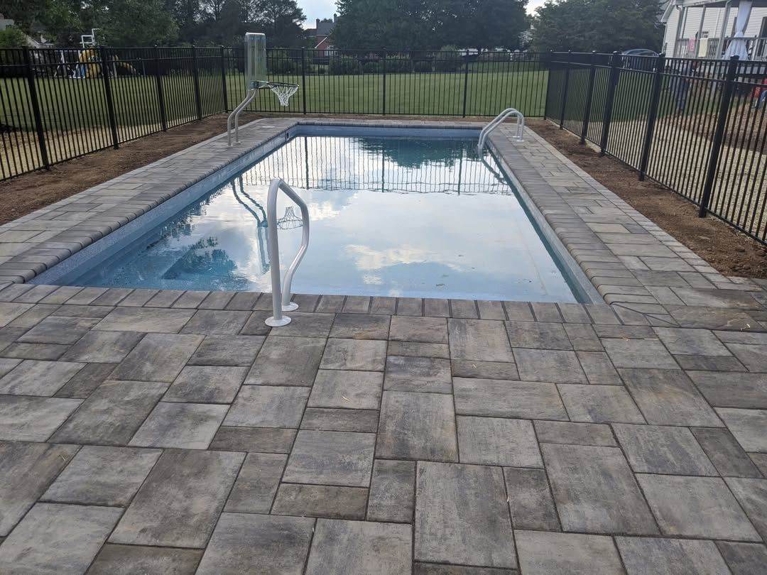 Jesse James Hardscaping - A rectangular swimming pool with brick patio. A metal fence encloses the yard.