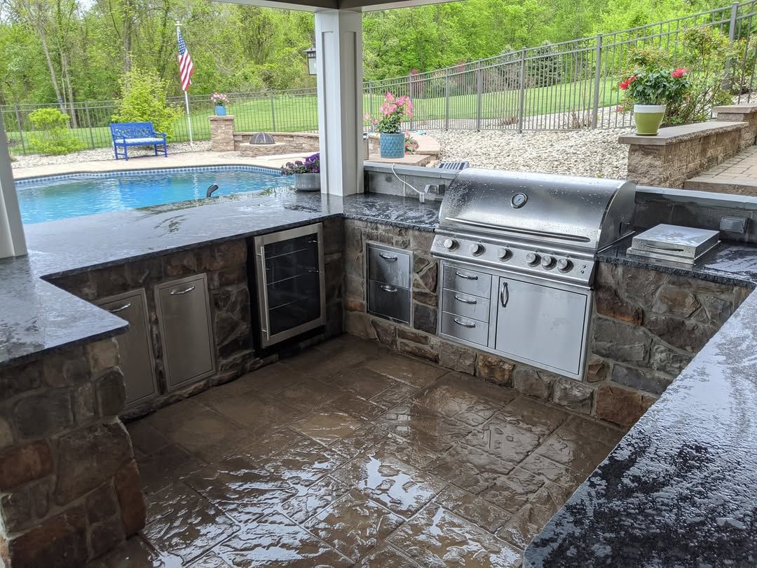Jesse James Hardscaping - Outdoor kitchen with stainless steel grill, stone walls, next to a swimming pool.