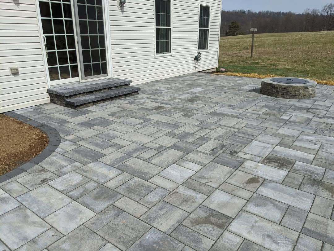 Jesse James Landscaping - Stone patio with steps and fire pit next to a white house.