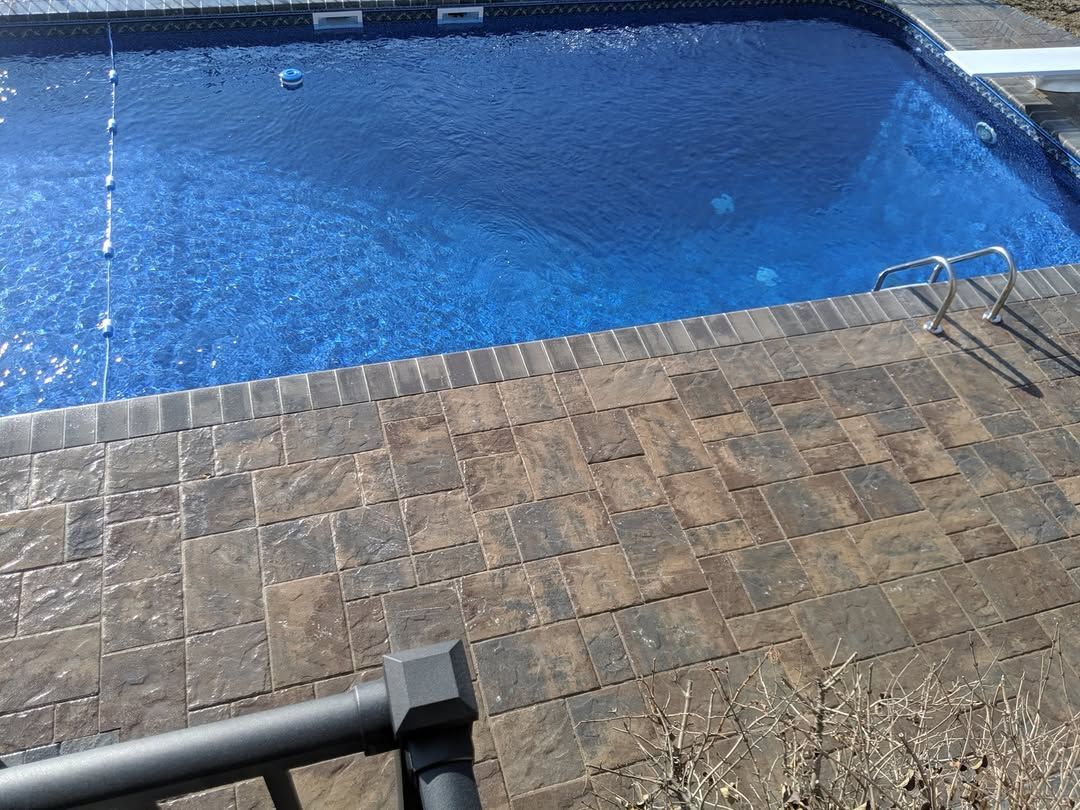 Jesse James Hardscaping - Pool with blue water and stone patio surrounding it.