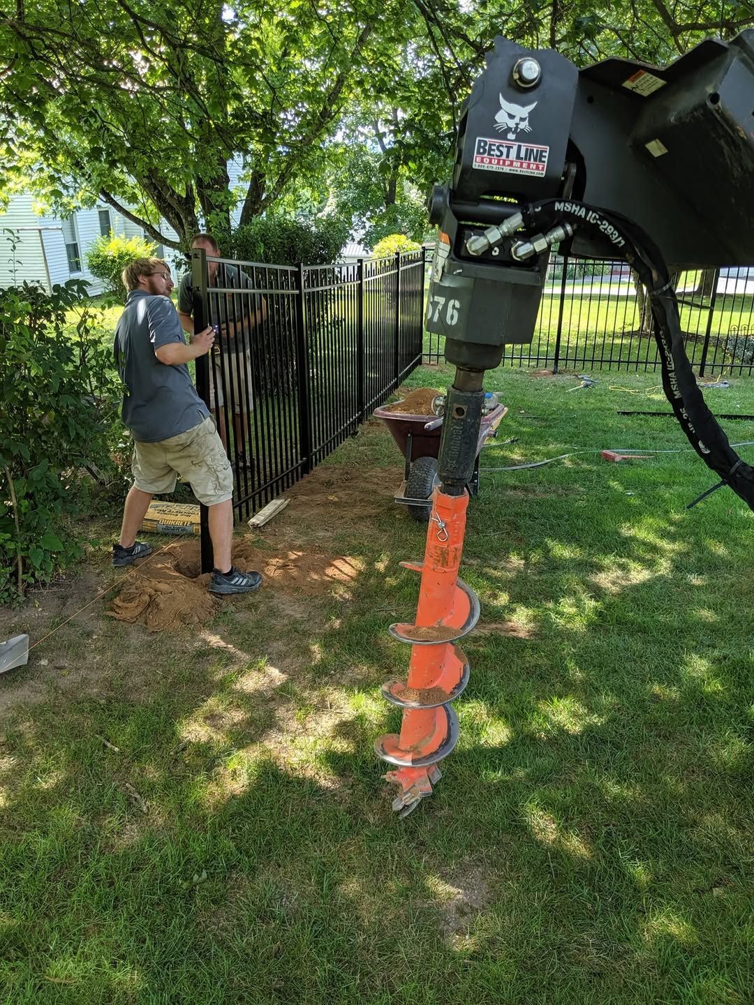 Jesse James Hardscaping - Image -Man using a Bobcat auger to drill holes for a black metal fence in a grassy yard.