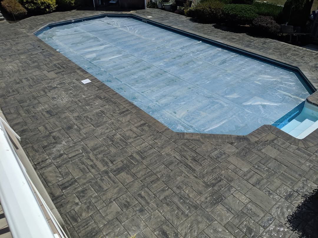 Jesse James Landscaping - Pool with a blue cover, surrounded by dark gray patterned pavers.
