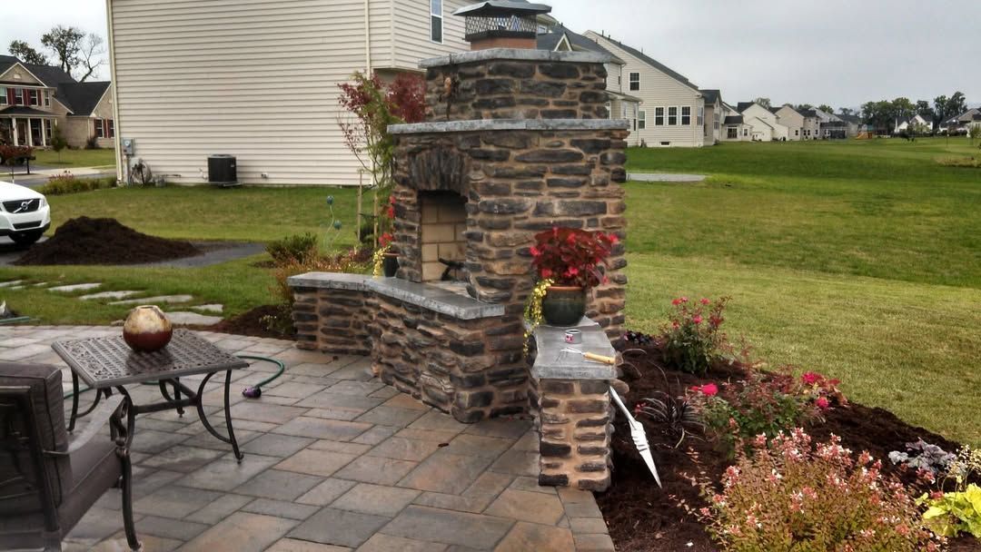 Jesse James Landscaping - Outdoor stone fireplace and patio with seating in a backyard.