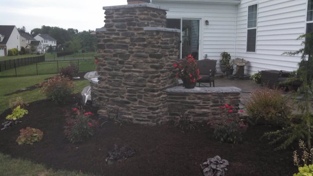 Jesse James Landscaping - Stone tiered water feature with patio, plants, and a white house.