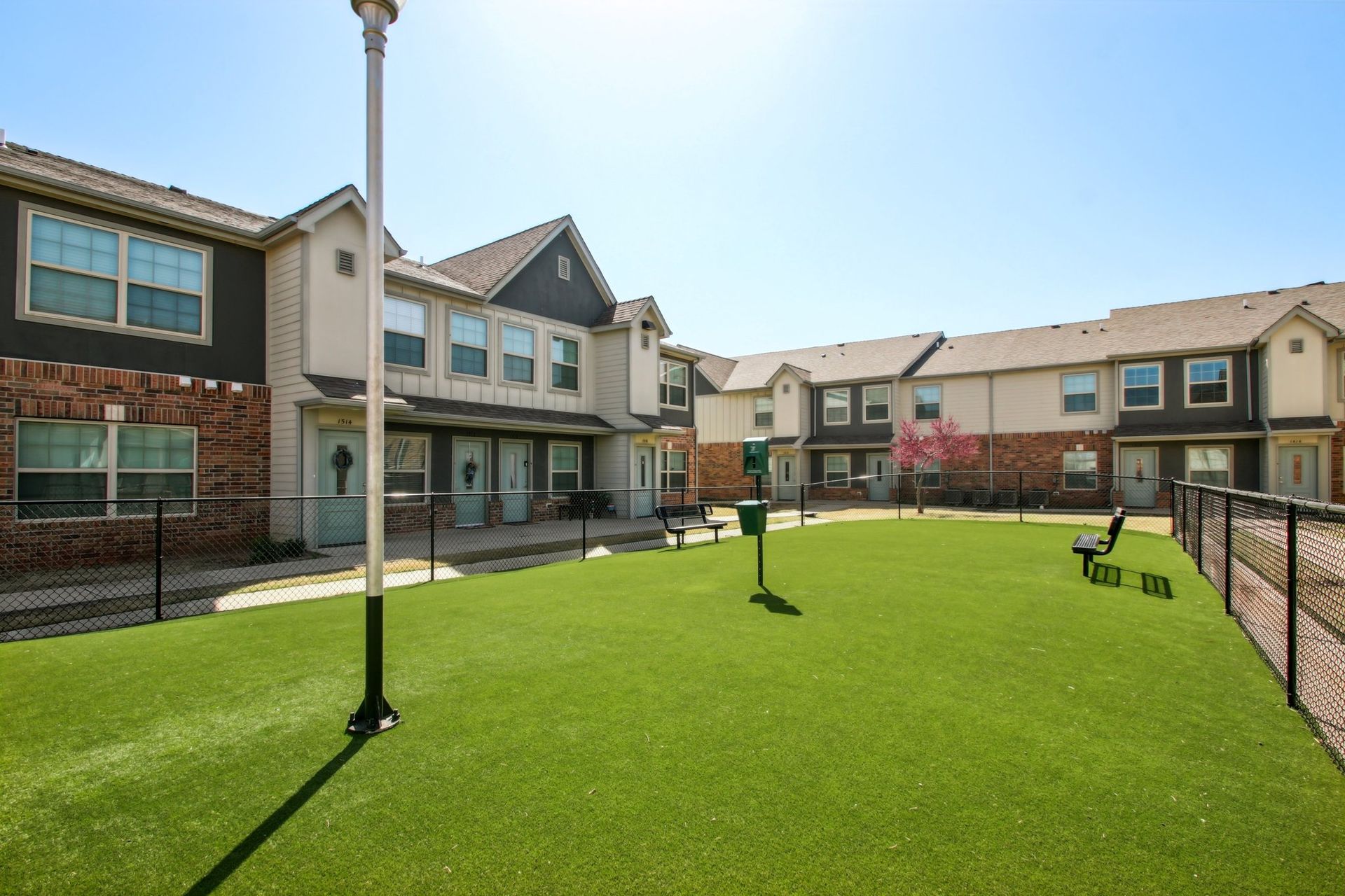 A fenced in dog park in front of a row of apartment buildings.