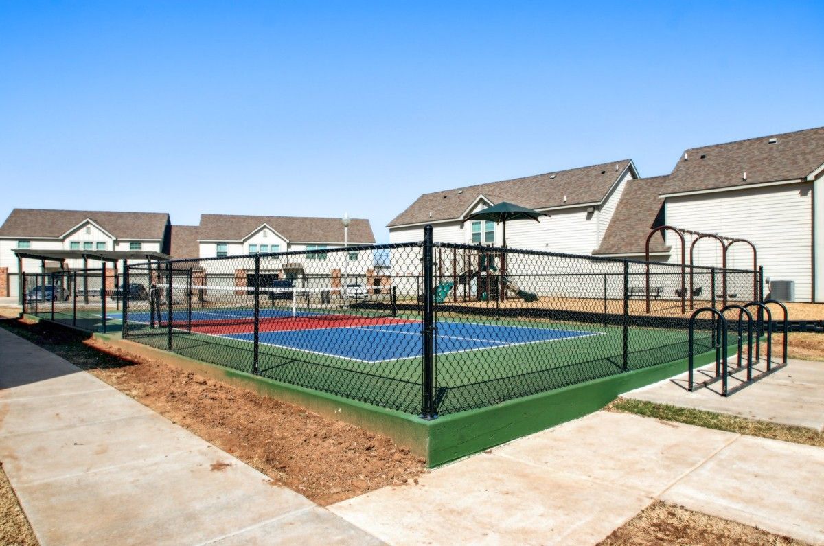 A basketball court with a chain link fence and a playground in front of a row of houses.