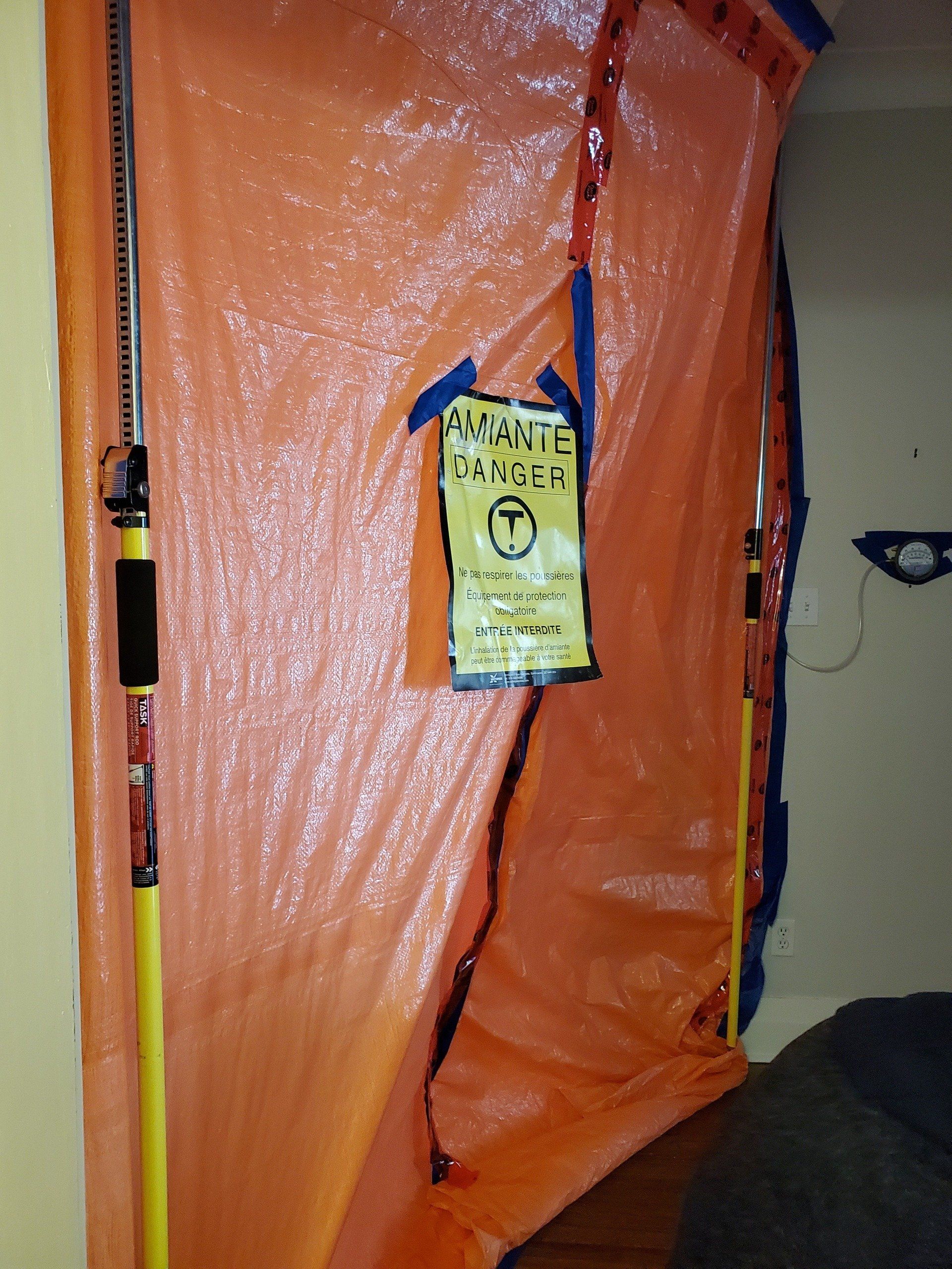 Barrière en plastique orange avec panneau d'avertissement, probablement pour des travaux de construction ou d'assainissement, installée dans une porte.