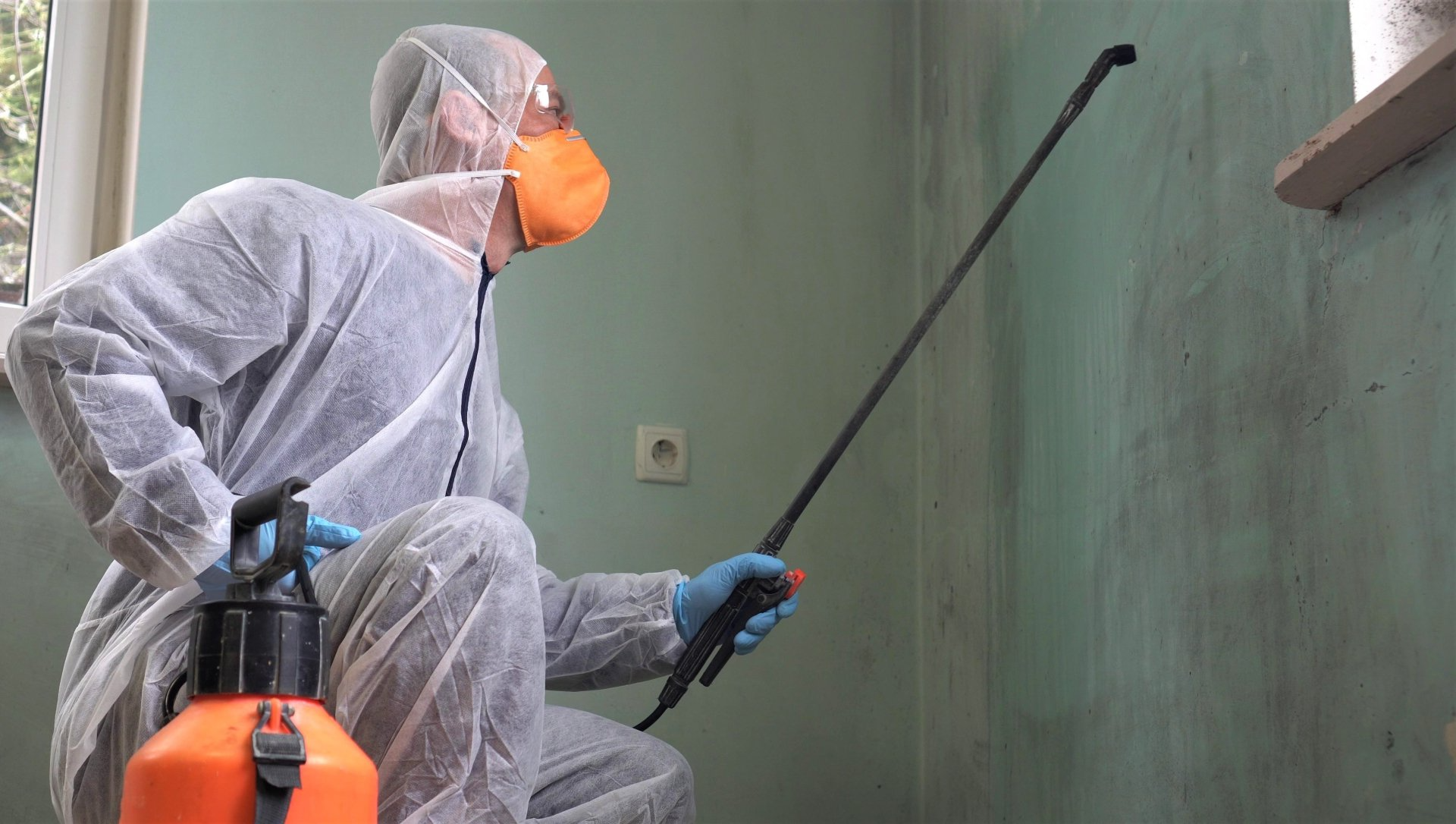 Un homme en combinaison de protection pulvérise un mur avec un pulvérisateur.