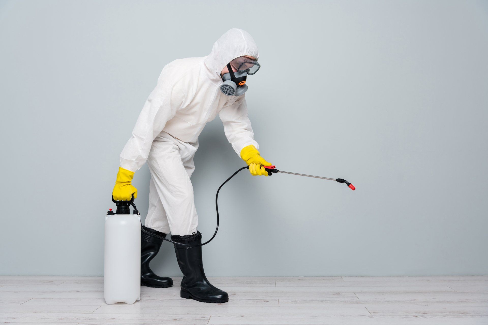 A man in a protective suit is spraying a wall with a sprayer.