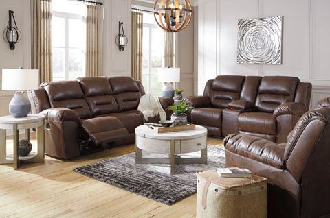 A living room with brown leather reclining furniture, including a sofa, loveseat, and armchair, arranged around a circular coffee table.