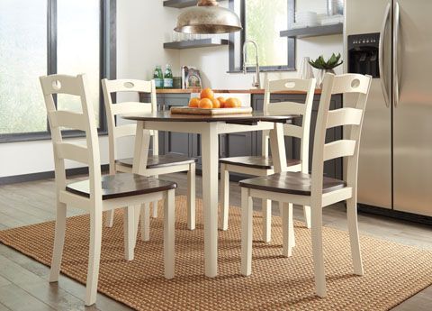 A round dining table with four chairs in a kitchen setting. The table has a dark top with white legs and chairs.