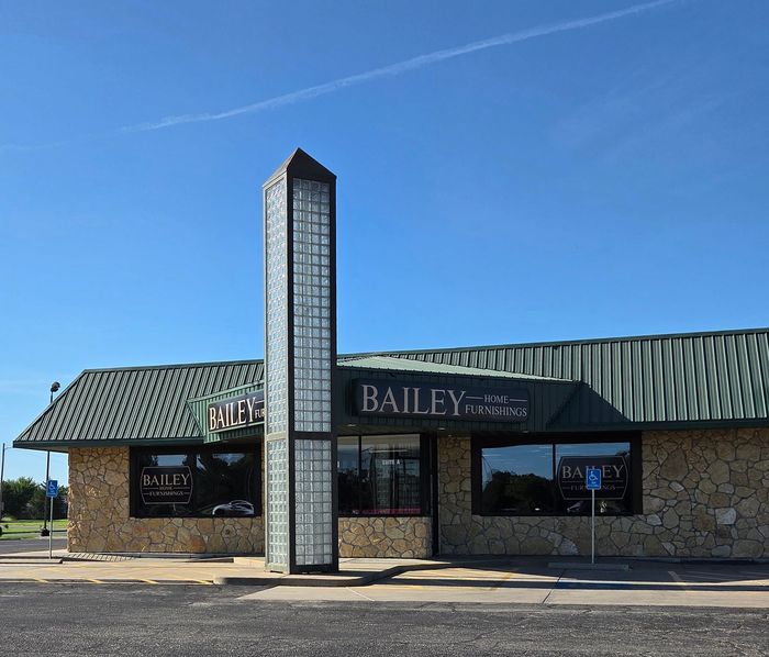 Bailey Home Furnishings exterior with a tall, glass-block tower. Building has green roof and stone facade with large windows.