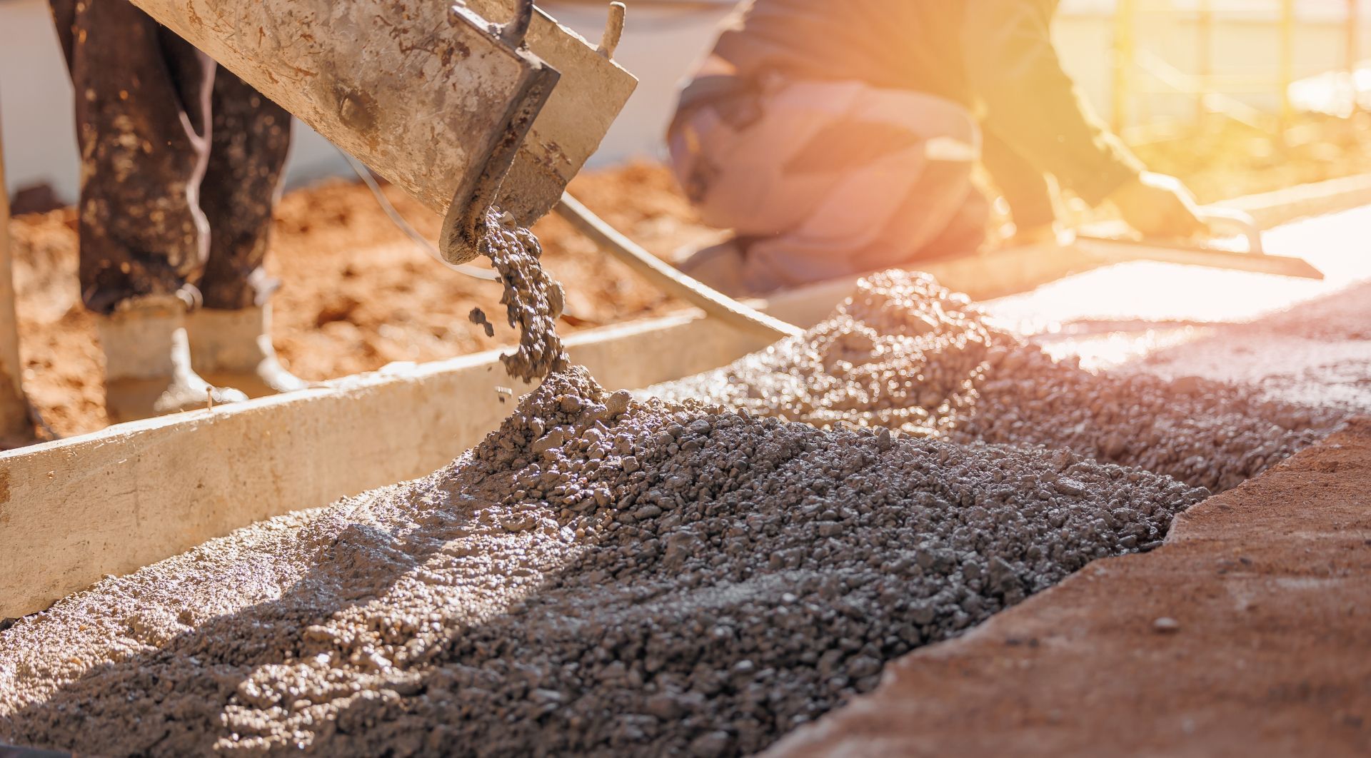 Concrete pouring from a chute at a construction site in warm sunlight