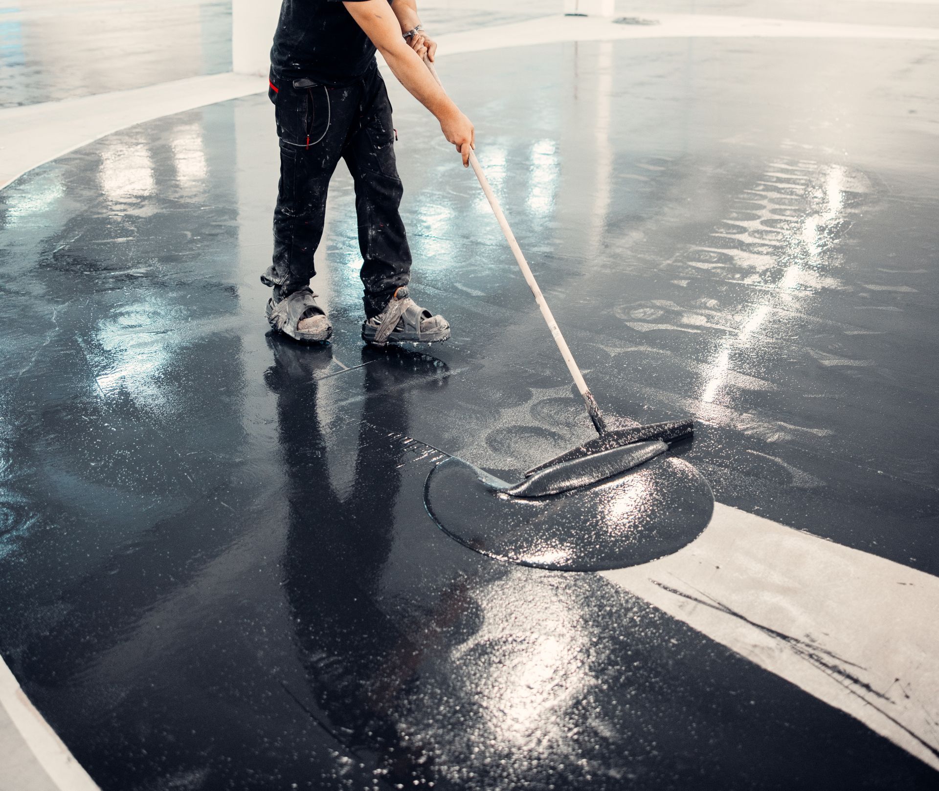 Person squeegeeing water from a dark wet floor with a long-handled mop in a bright indoor space