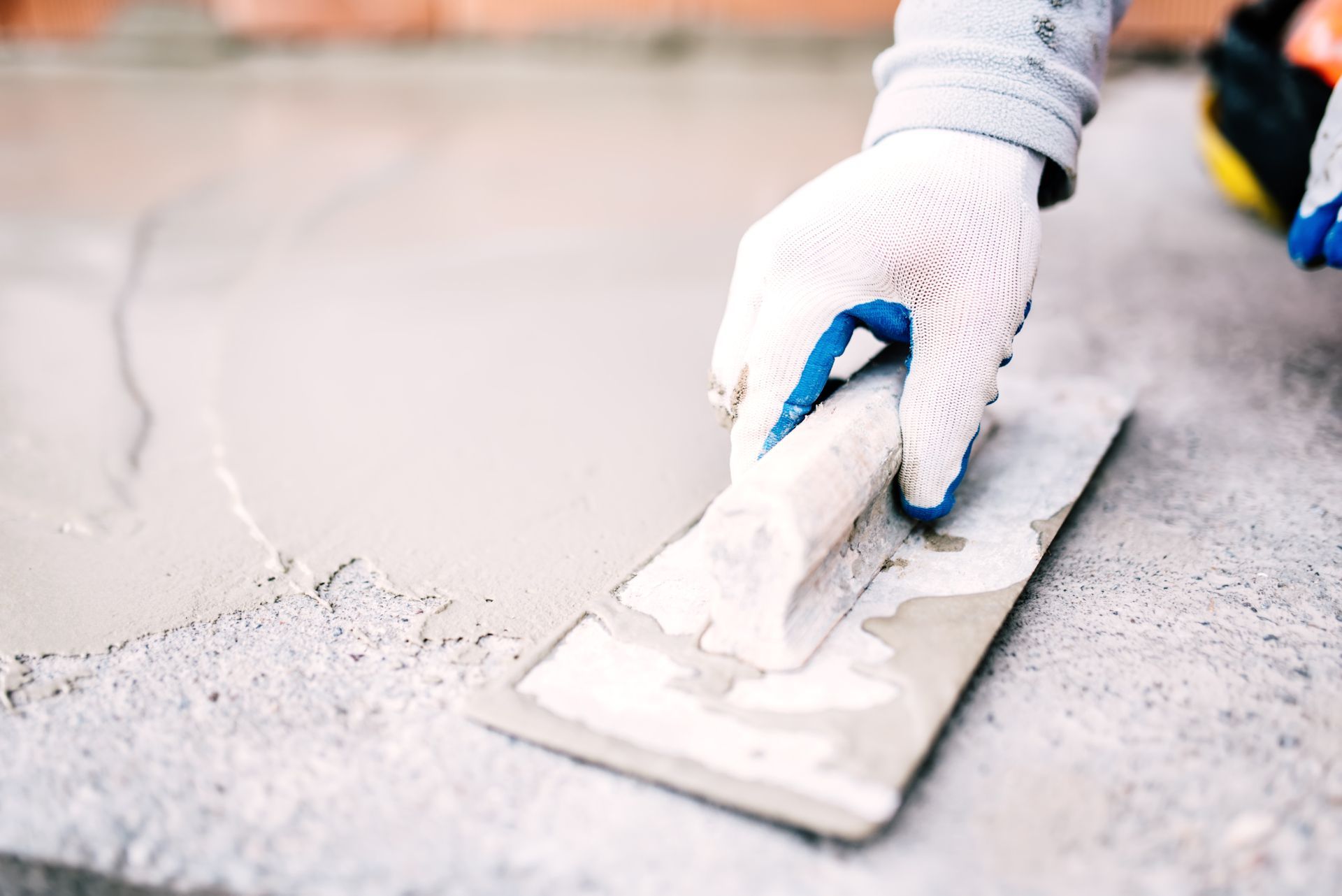 Hand using a trowel to smooth wet concrete on a floor surface
