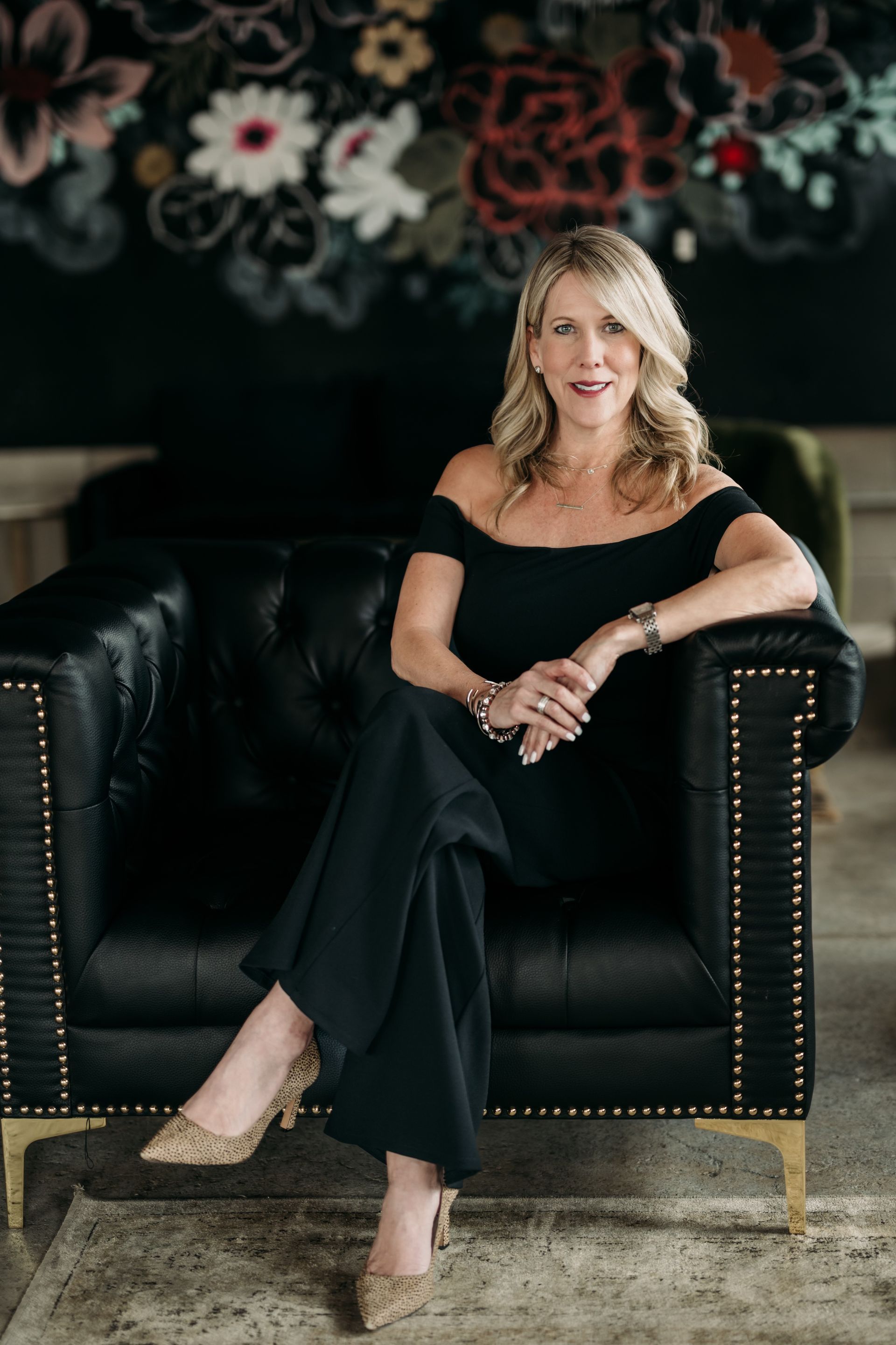 A woman is sitting at a desk with a laptop and a vase of flowers.